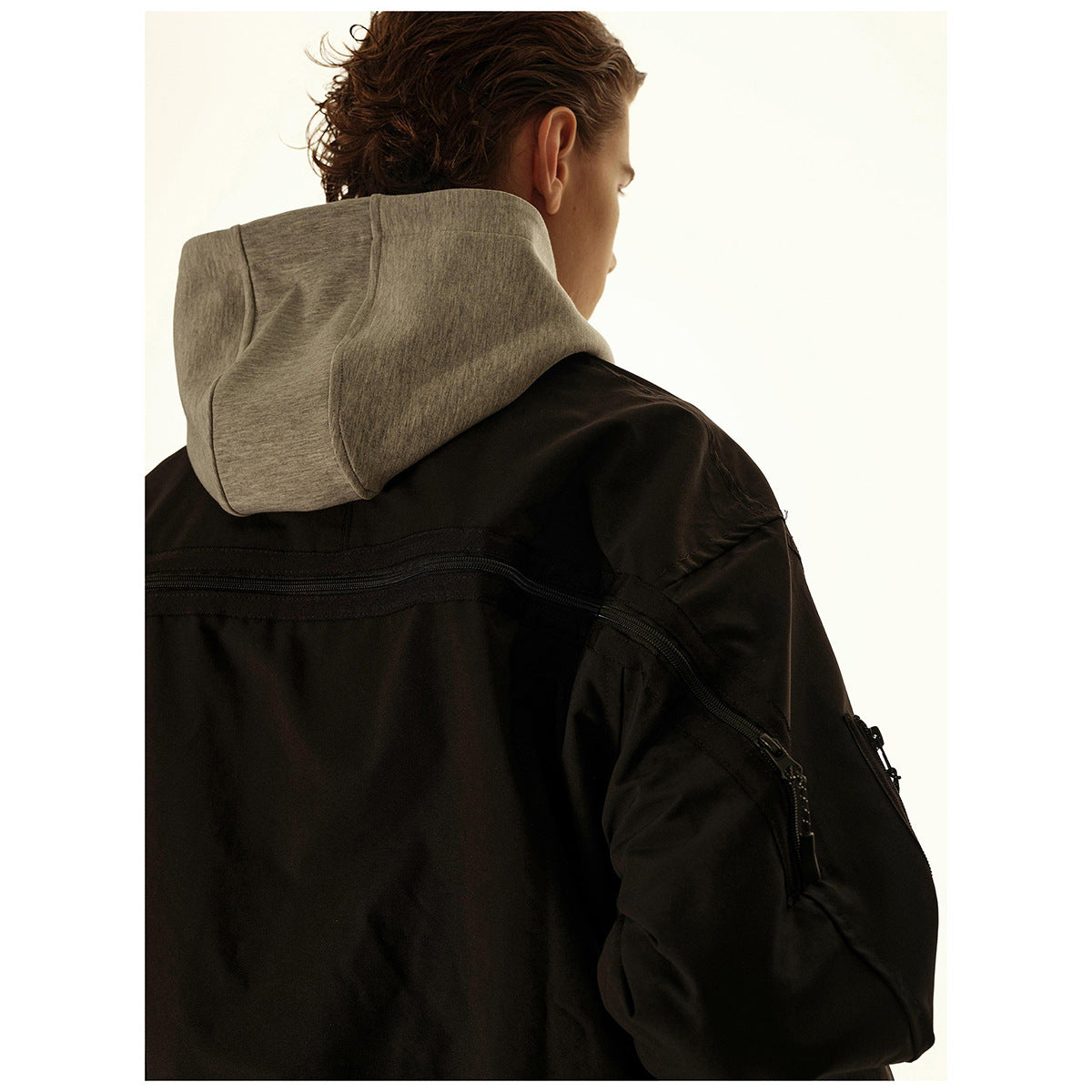 Close rear view of a black bomber jacket with a gray hood and a curved zipper detail across the back.