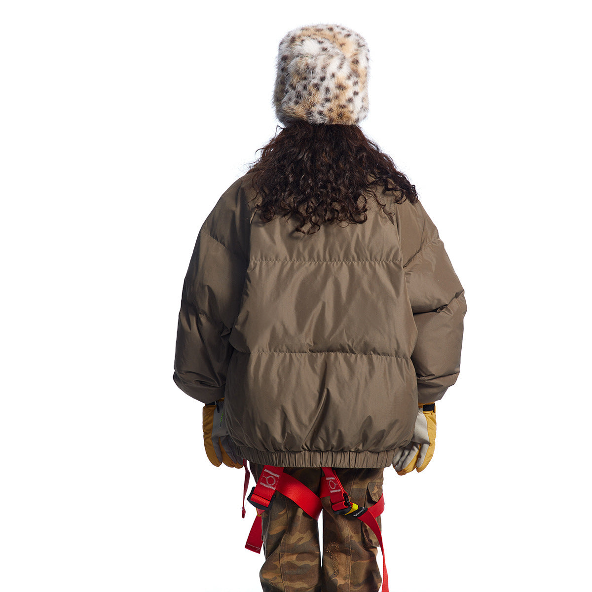 Rear view of a model wearing a taupe puffer jacket with a gathered hem and voluminous sleeves.