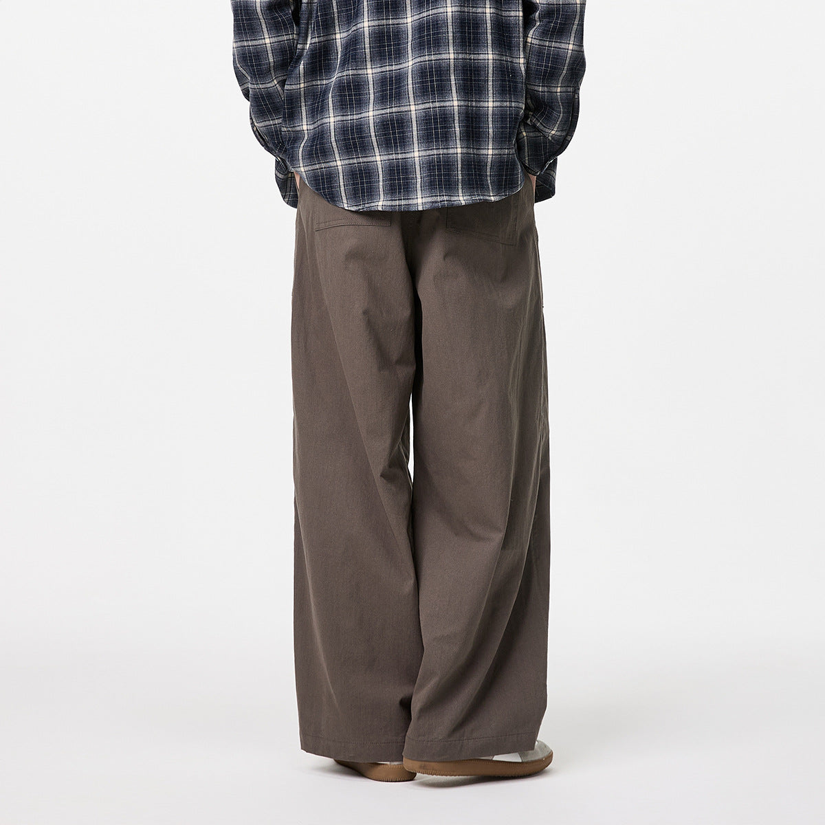 Rear view of a model wearing loose, dark taupe wide-leg trousers with back pockets and a navy plaid shirt.