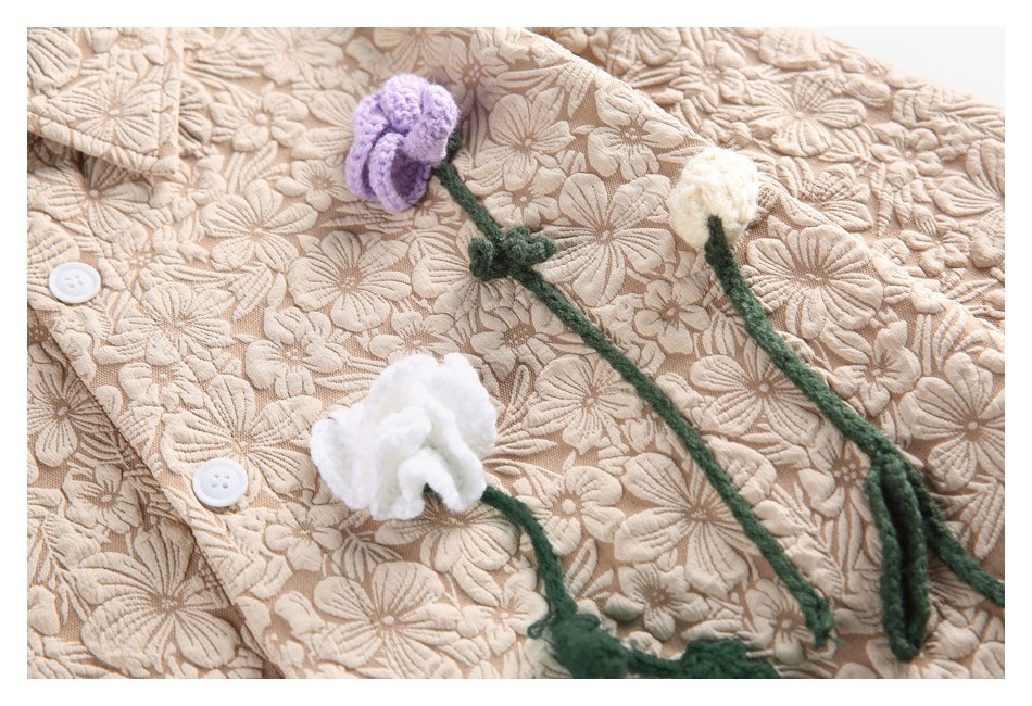 Close-up of raised purple and white yarn flowers with green stems on a beige floral-textured garment.