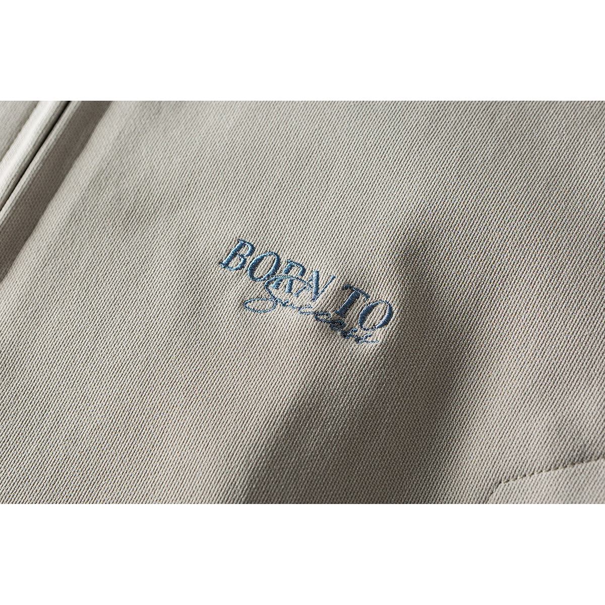 Close-up of blue embroidered lettering on the beige jacket.