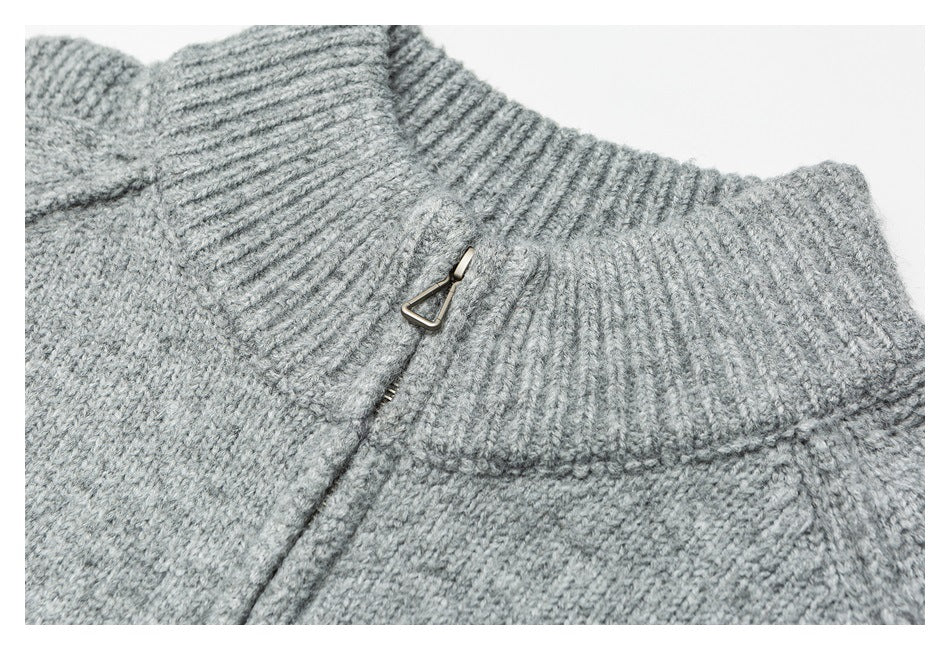 Close-up of a light gray sweater's ribbed high collar and small metal zipper pull.