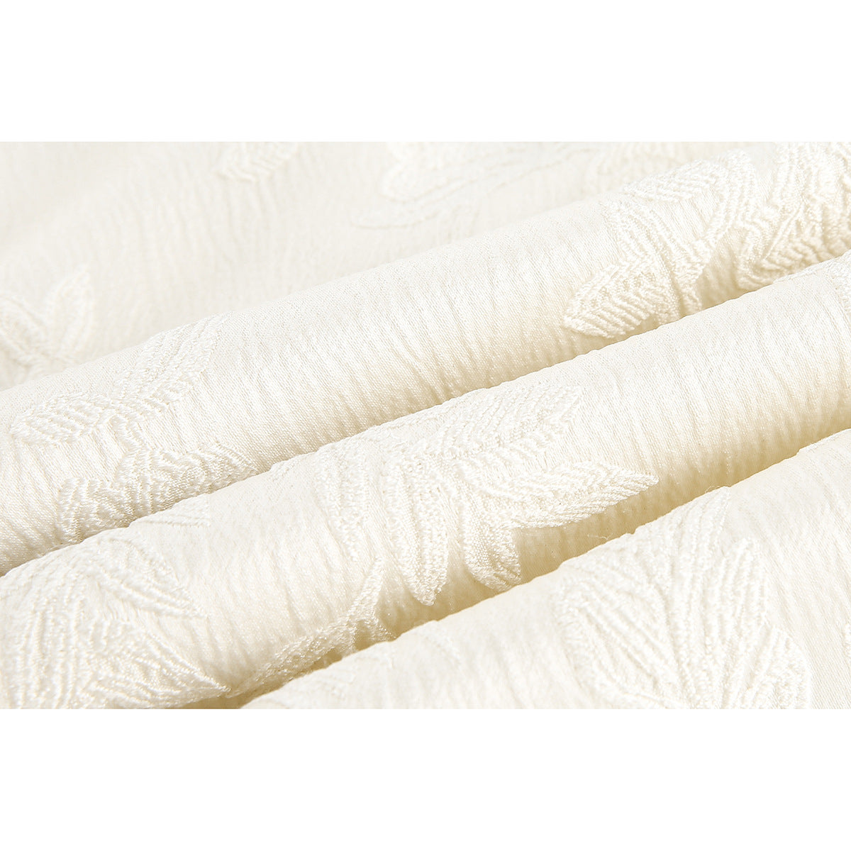 Close-up of ivory fabric with raised floral embroidery and a subtle woven texture.