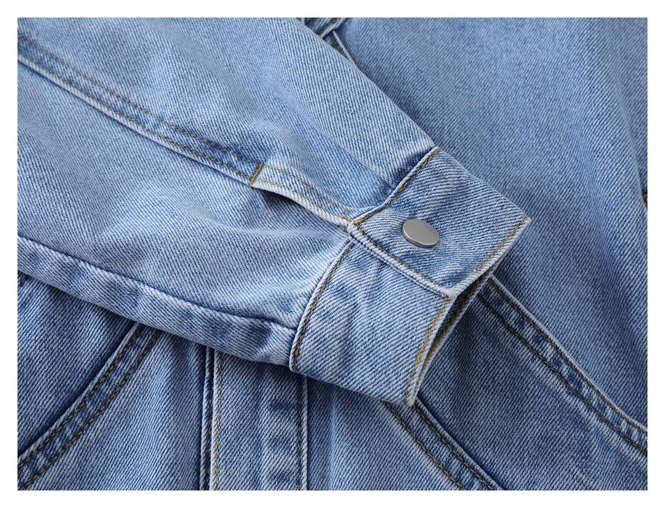 Close-up of light blue denim with stitched seams and a silver snap on a folded tab.