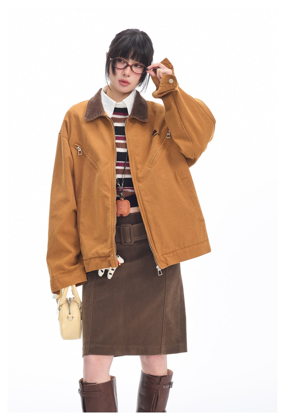 Model wearing a mustard zip jacket with a brown collar over a striped top and brown skirt.
