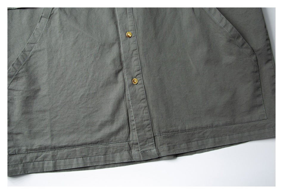 Partial flat-lay lower front of a dark gray-green shirt with tan buttons, large pockets, and a stitched hem.