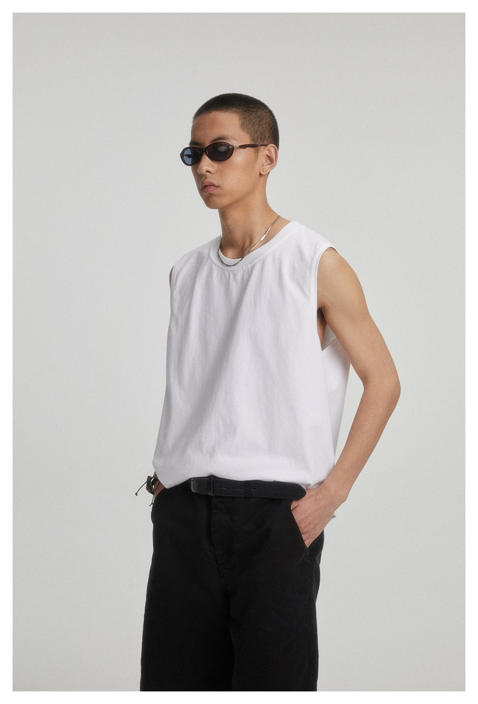 Three-quarter view of a model wearing a plain white sleeveless crew-neck shirt and black shorts.