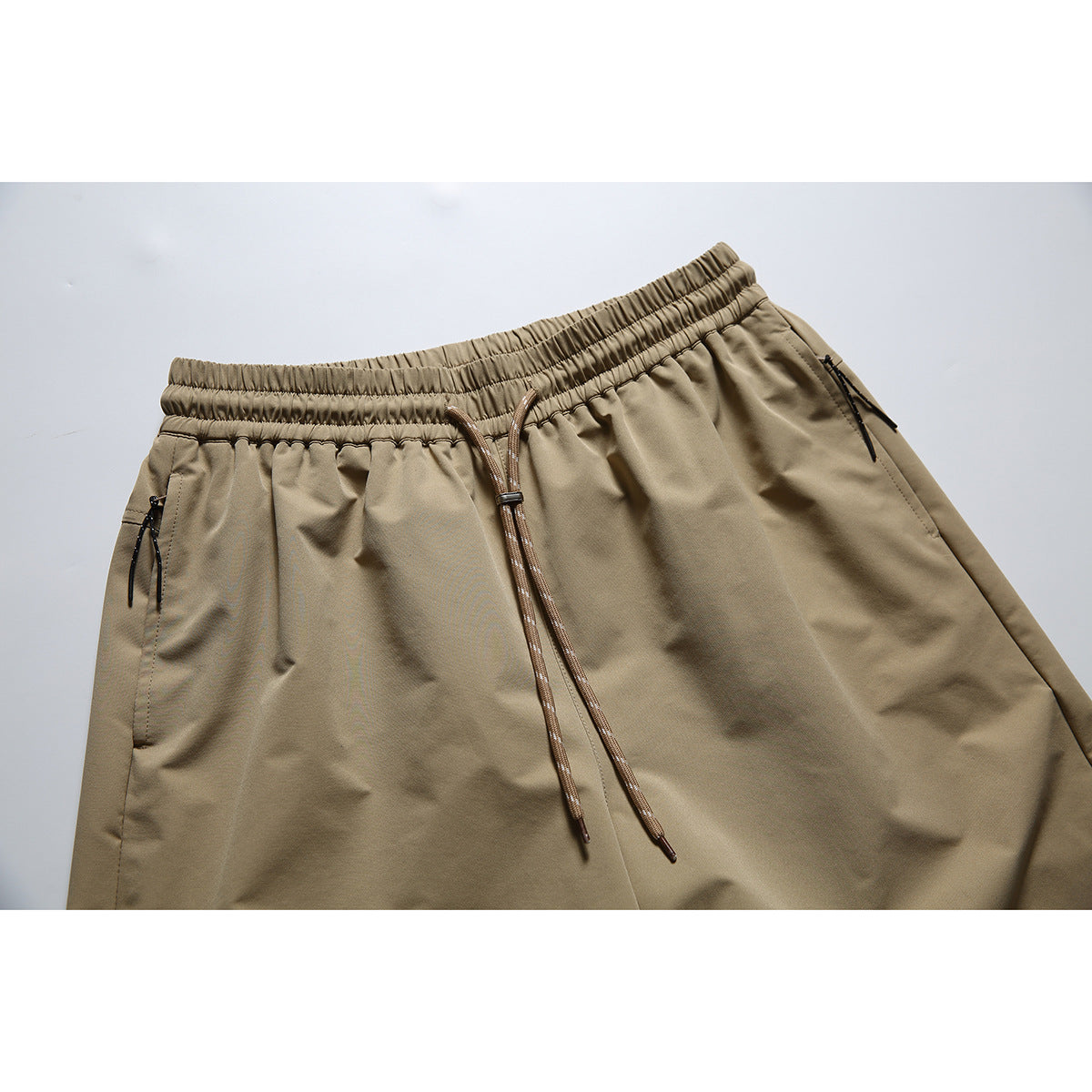Close-up of khaki shorts showing the elastic waistband, long drawstring and zippered pockets.