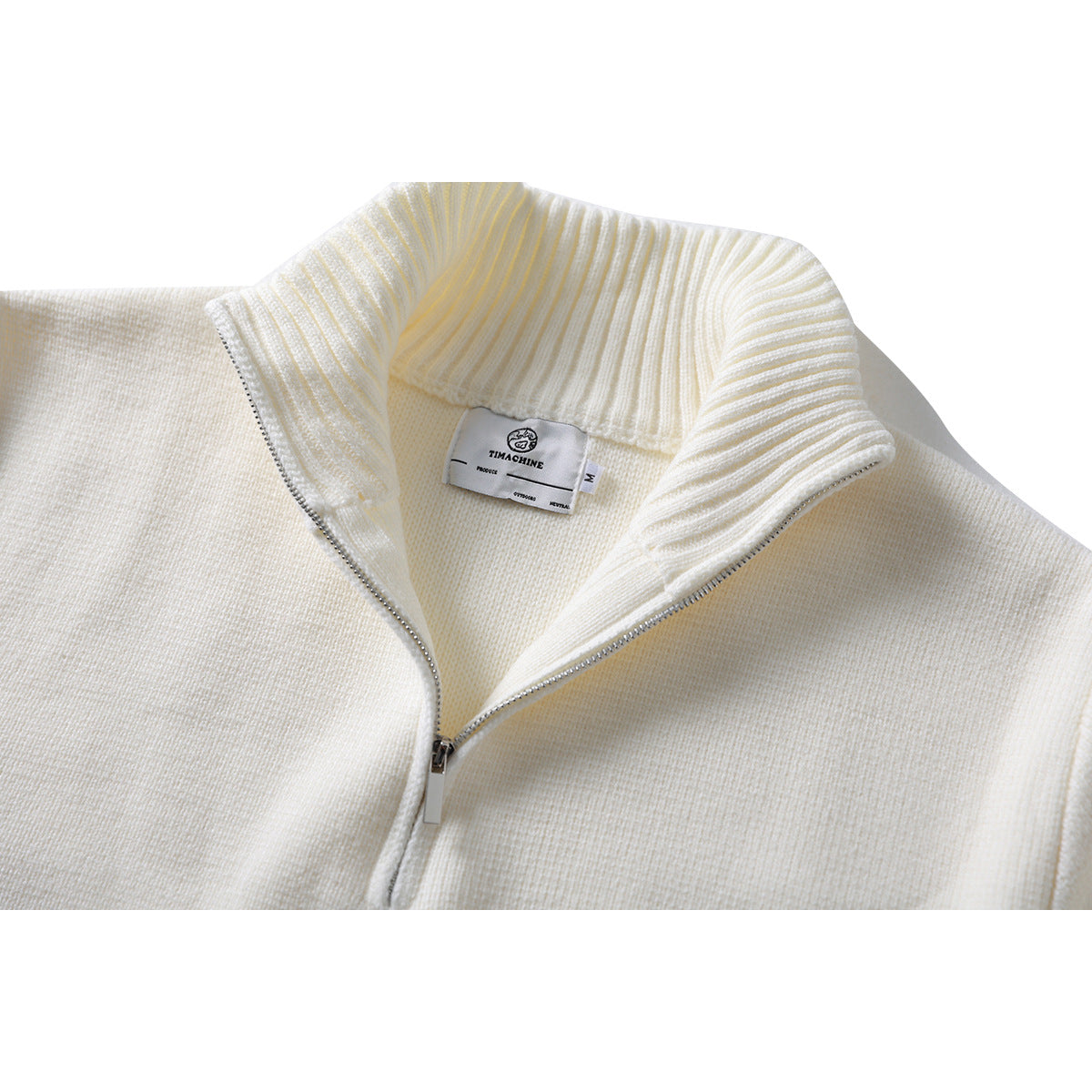 Close-up of an ivory quarter-zip knit sweater showing its ribbed collar, silver zipper, and neck label.