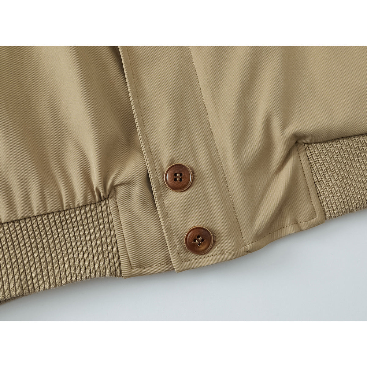 Close-up of a tan jacket’s two brown buttons, front placket, and ribbed hem.