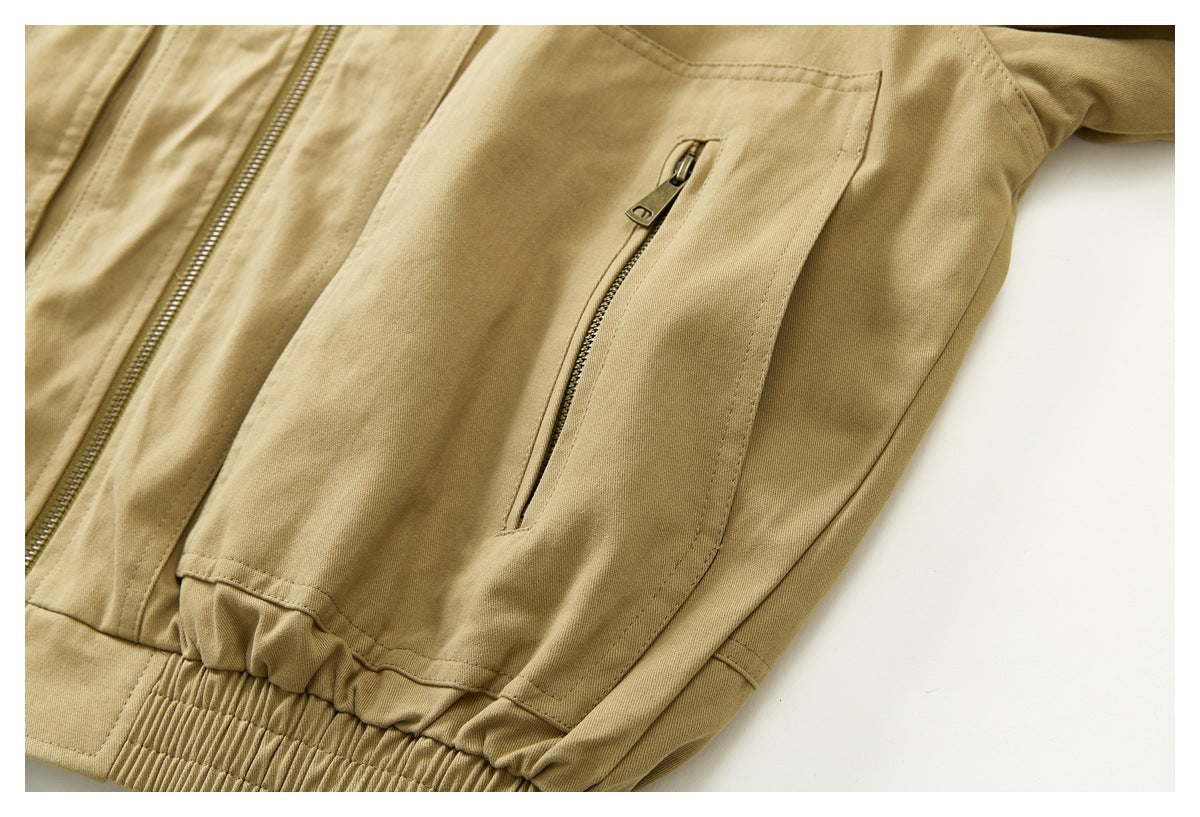 Close-up of a tan jacket's angled zip pocket, front zipper, and gathered waistband.