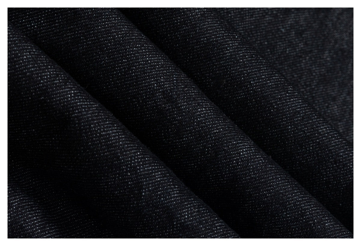 Close-up of dark black woven fabric with a fine, subtly speckled texture and diagonal folds.