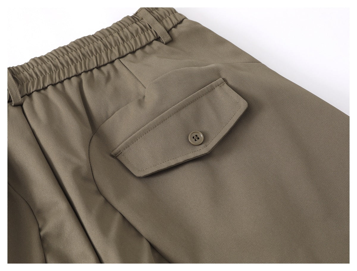 Close-up of olive-taupe trousers showing the elastic waistband and a buttoned back pocket.