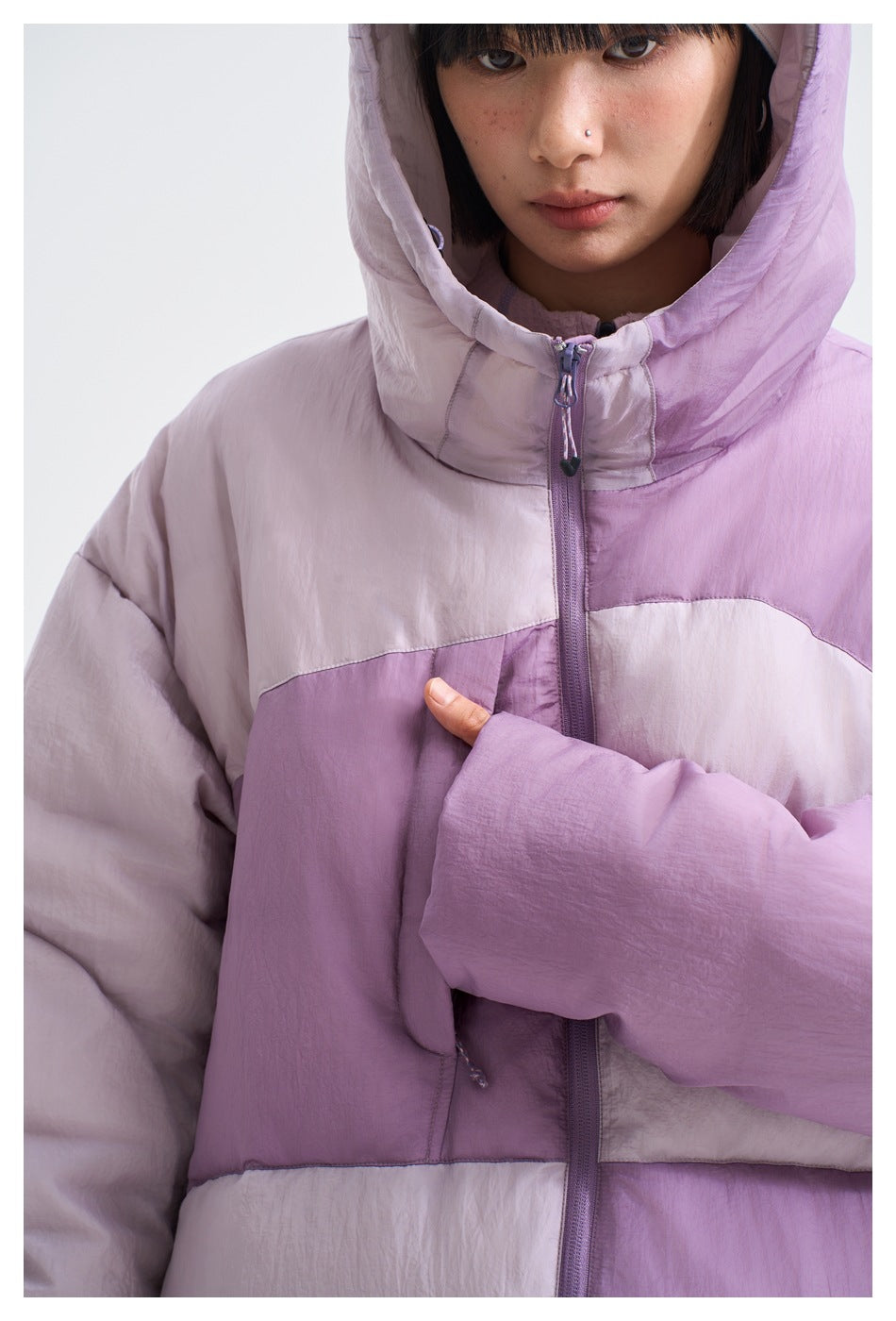 Close-up of a lavender color-block puffer jacket showing its hood, front zipper, and fabric panels.