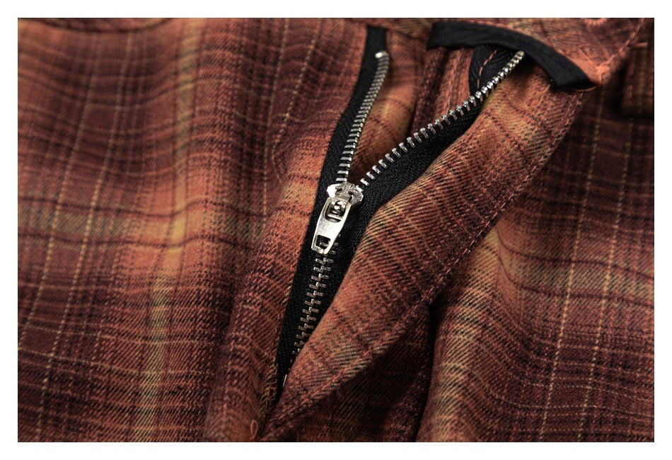 Close-up of the metal zipper fly on brown and tan plaid trousers.