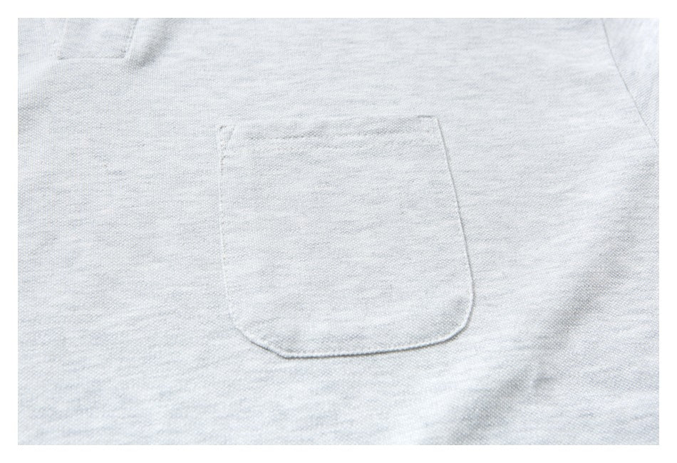 Close-up of a rectangular patch pocket on light gray shirt fabric.