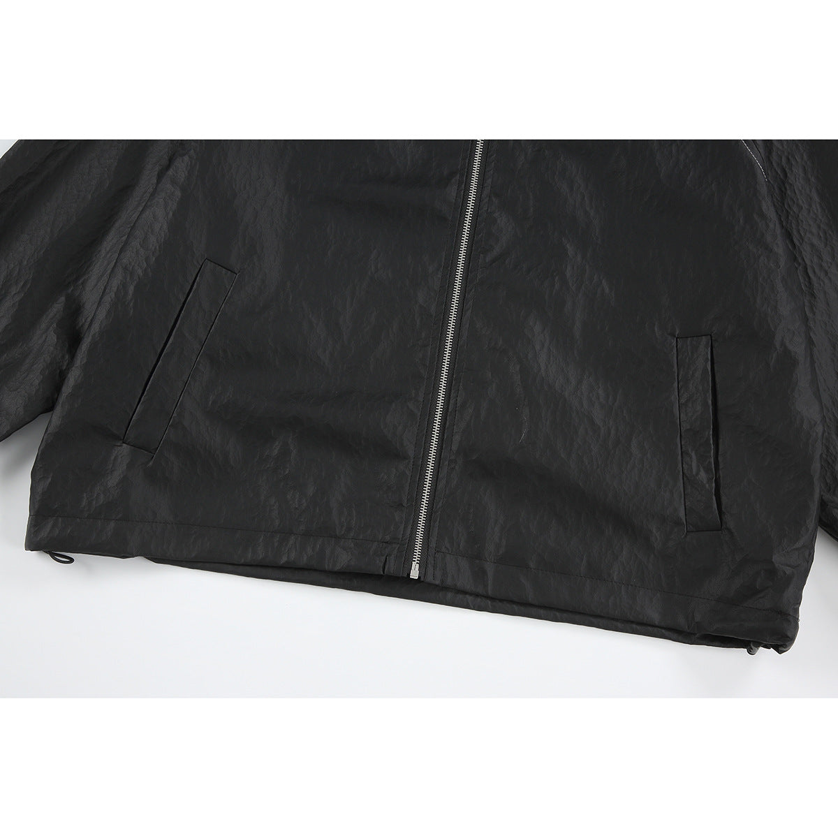 Close-up of the lower front of a black jacket, showing two slanted pockets, a silver zipper, and hem.