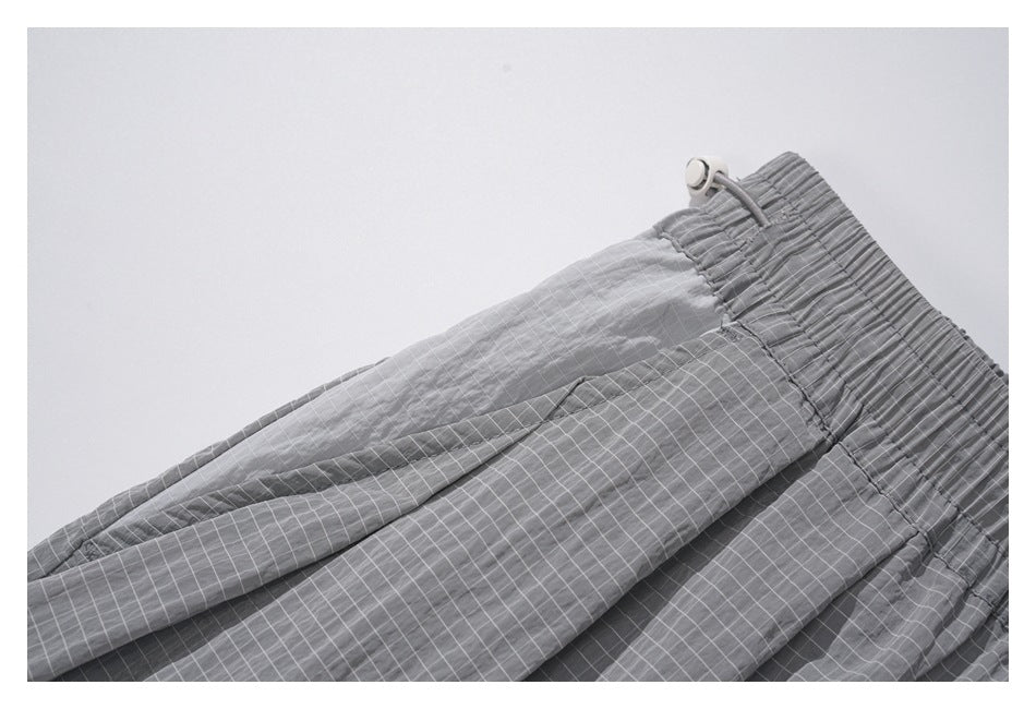 Close-up of gray grid-pattern trousers showing the gathered elastic waistband and drawstring.
