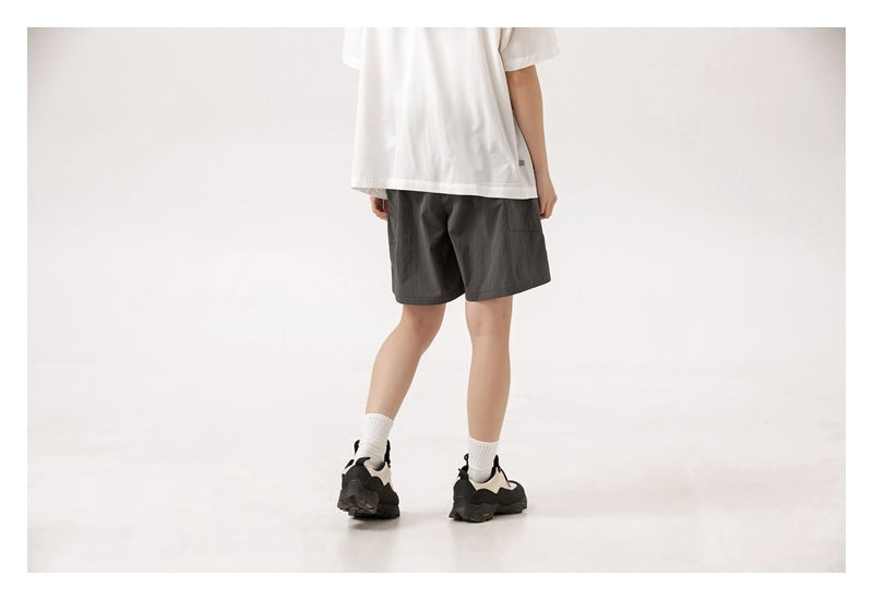 Rear view of a person wearing charcoal shorts with a white T-shirt, crew socks, and black sneakers.