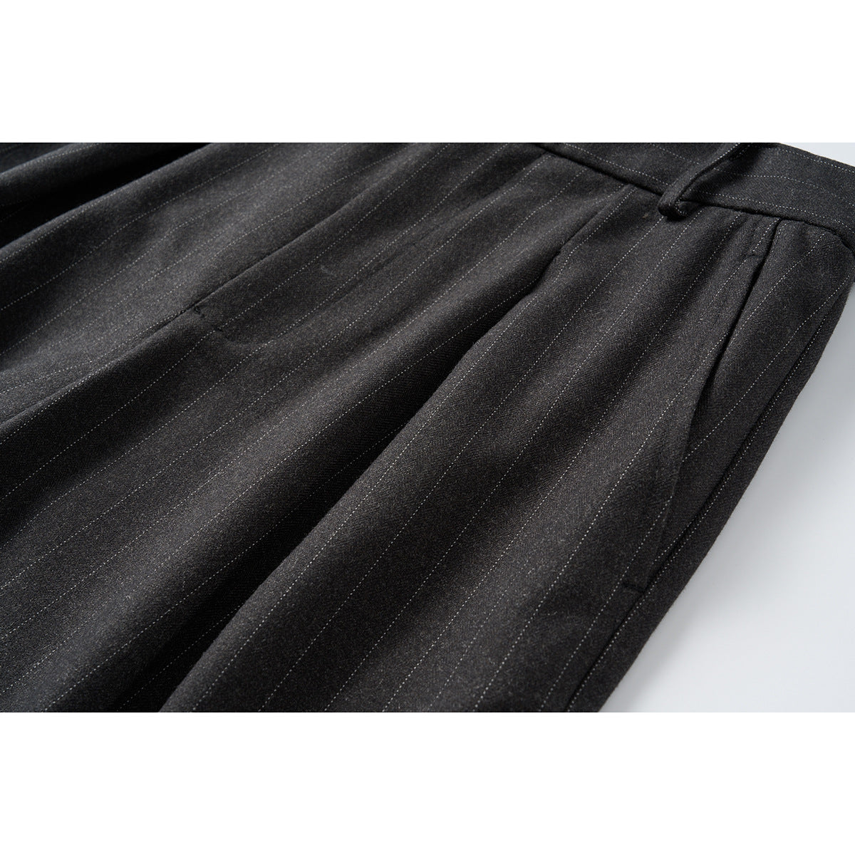 Close-up of charcoal pinstripe trouser fabric, front pleats and a side pocket opening.