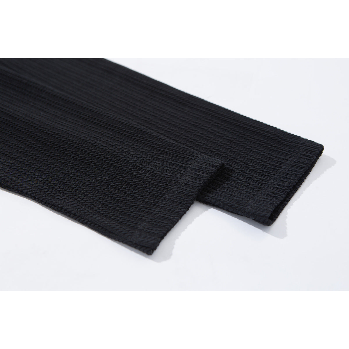Close-up of the black ribbed shirt's long sleeve and stitched cuff on a white background.