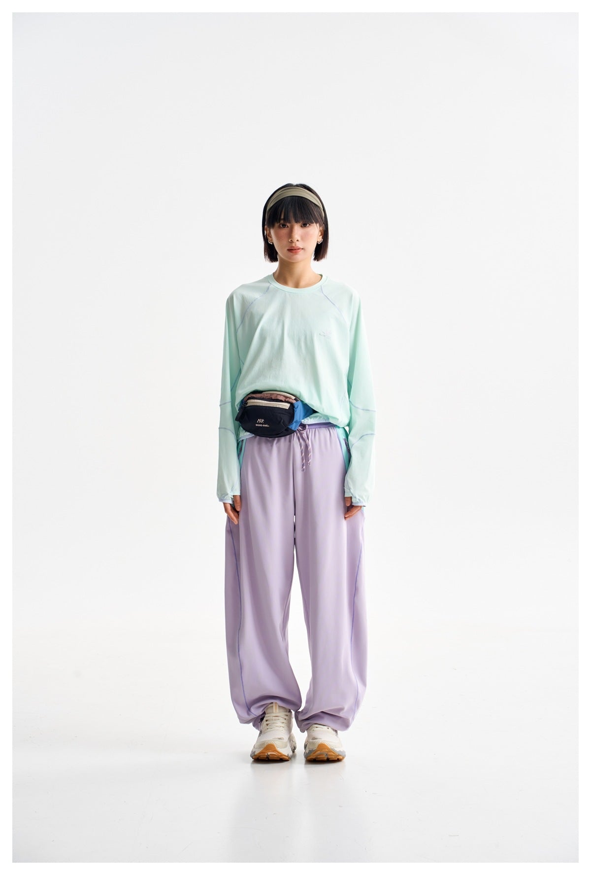 A woman models a mint long-sleeve top and loose lavender trousers against a plain white studio background.