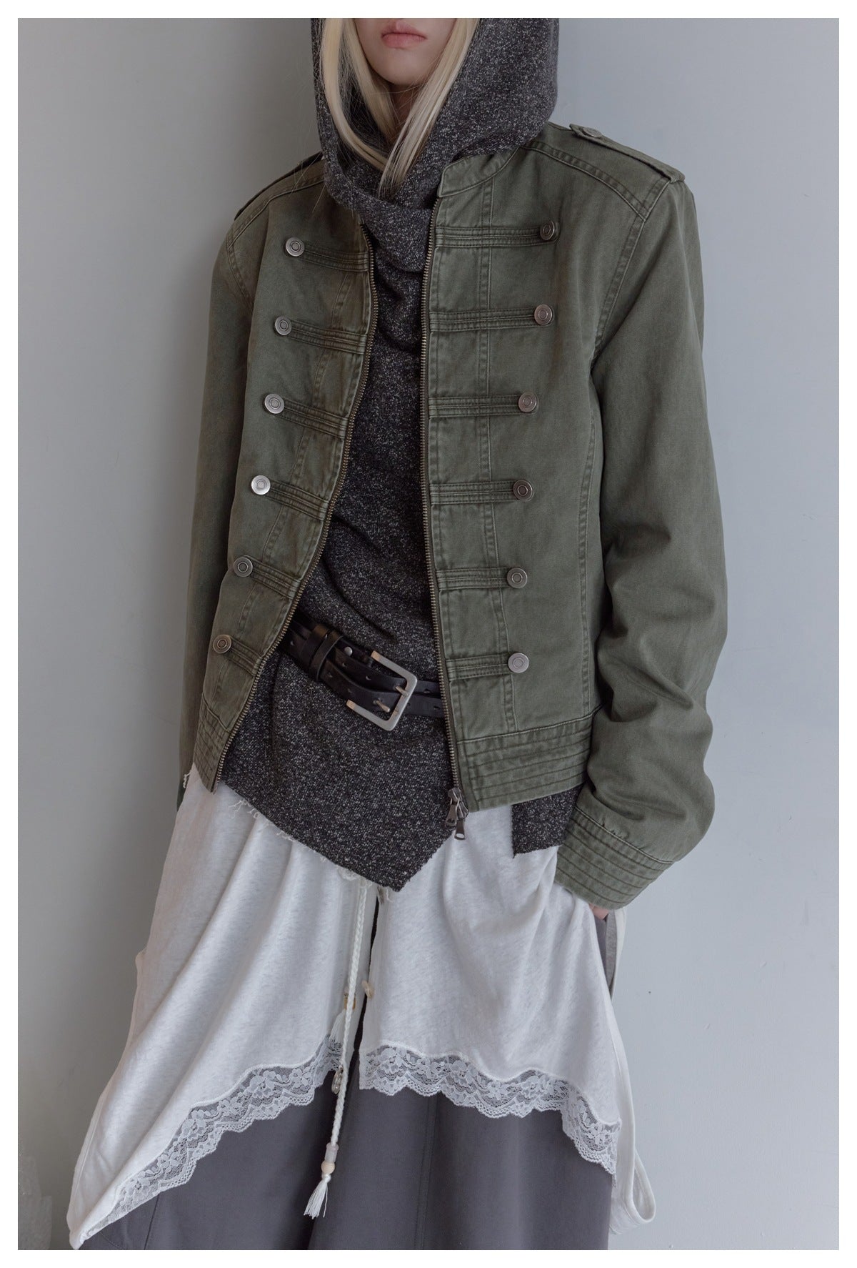 Close view of an olive jacket with rows of decorative buttons, stitched panels, and a front zipper.