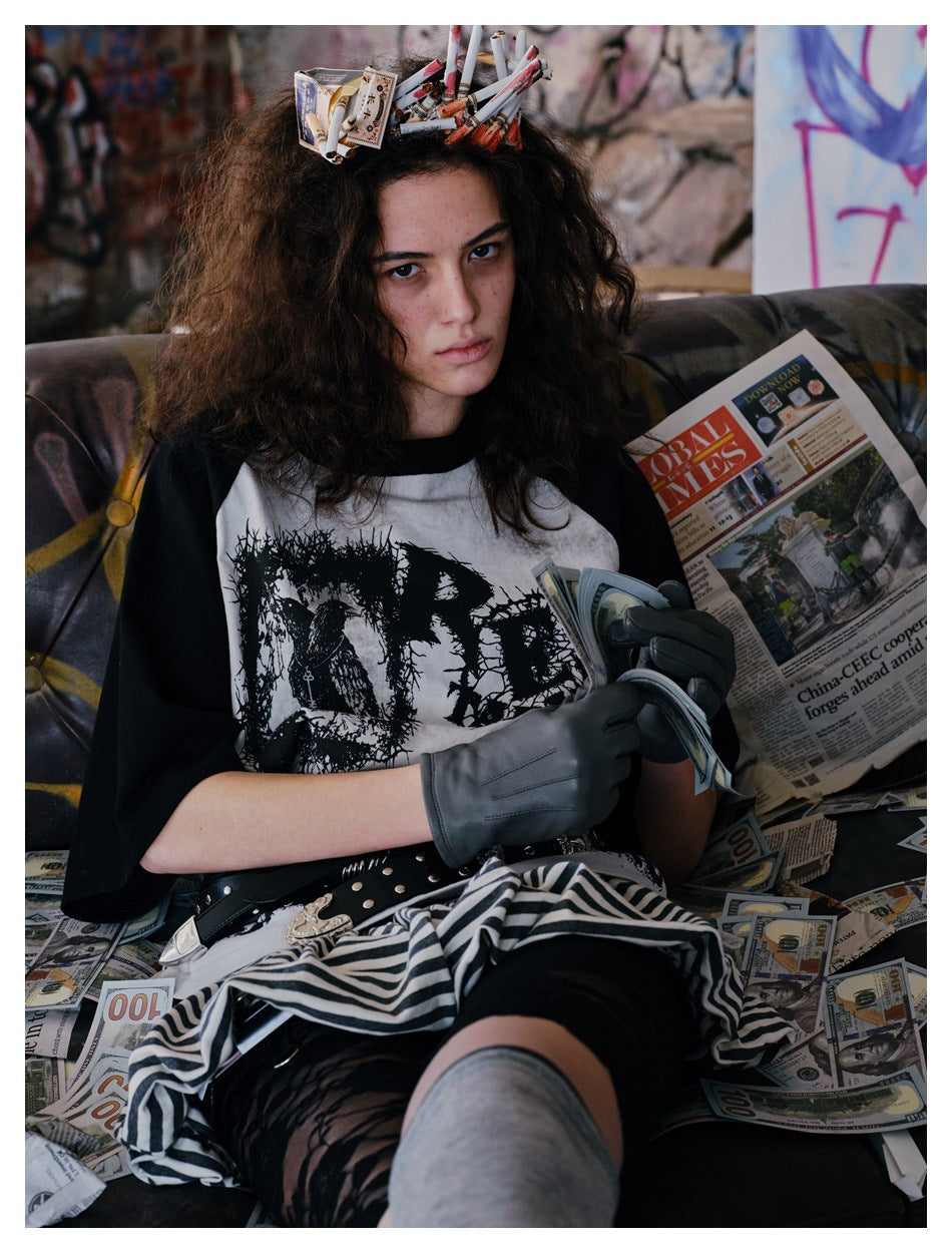 Model seated in a graphic black-and-white raglan T-shirt, striped skirt, gloves and thigh-high socks.