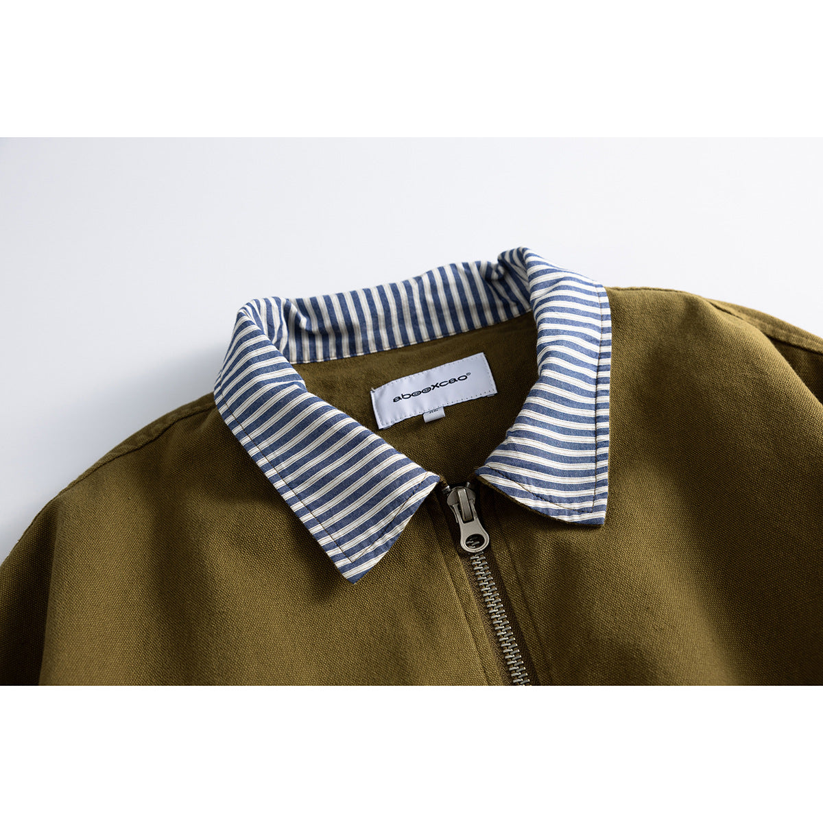 Close-up of an olive-brown jacket with a blue-and-white striped collar, front zipper, and sewn neck label.