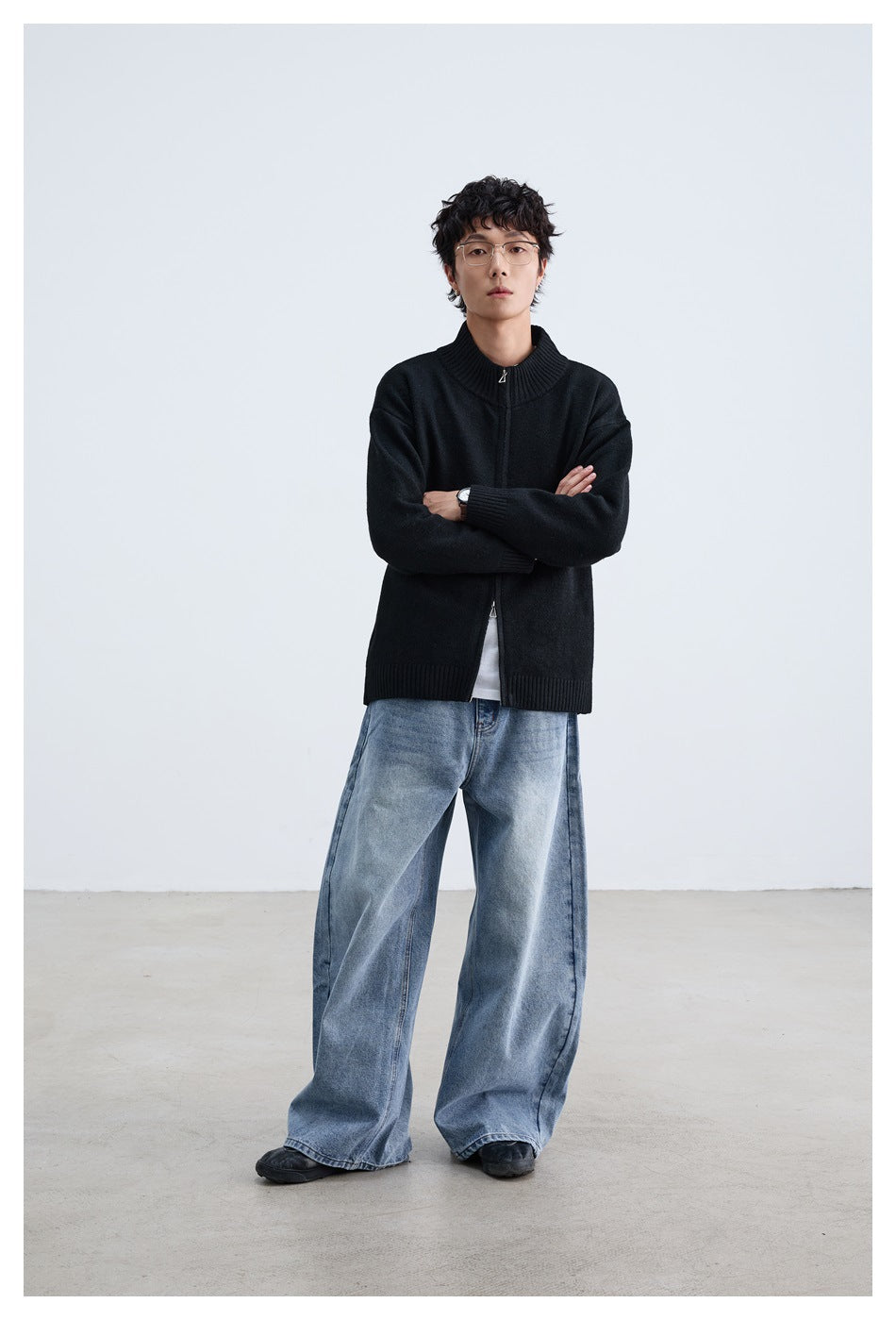 Model with arms crossed wearing a black zip-up knit cardigan, white tee and wide-leg light-wash jeans