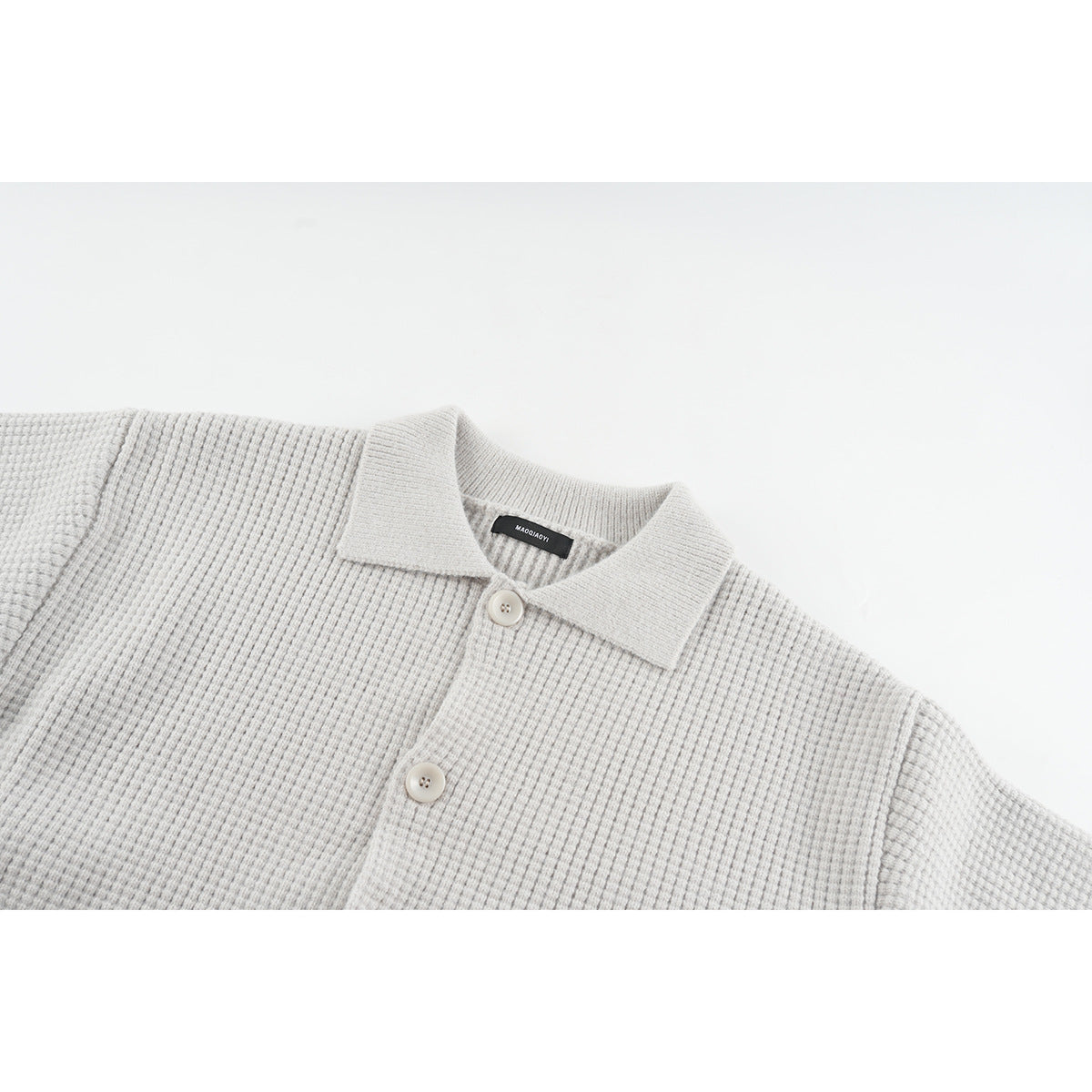Close-up of a light gray textured knit cardigan showing its pointed collar and front buttons.