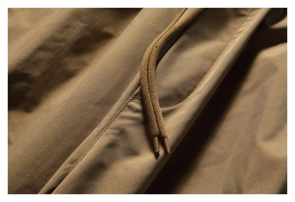 Close-up of the tan pants’ braided waist drawstrings and a curved pocket opening.