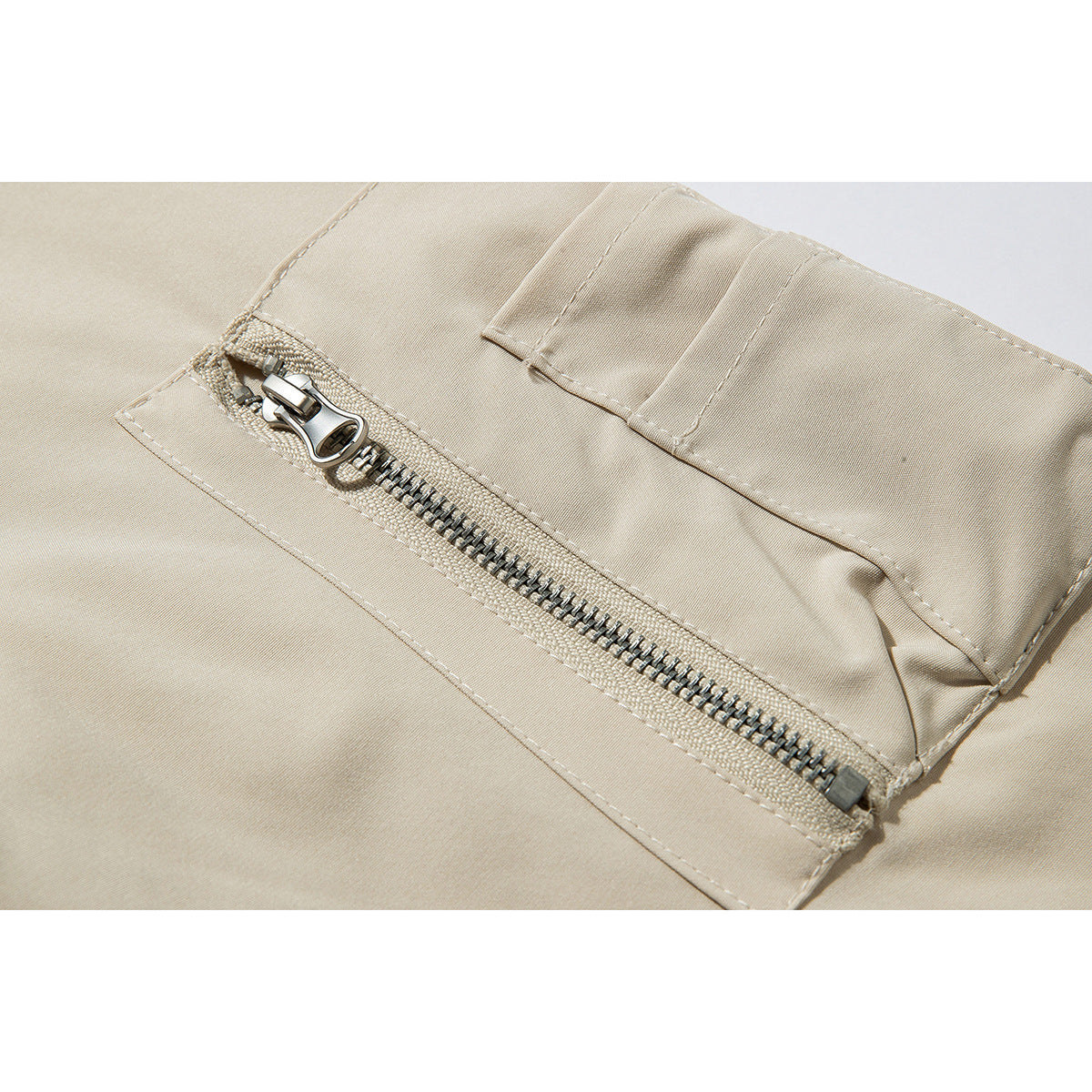 Close-up of a beige jacket’s zippered pocket with a metal zipper and stitched flap.