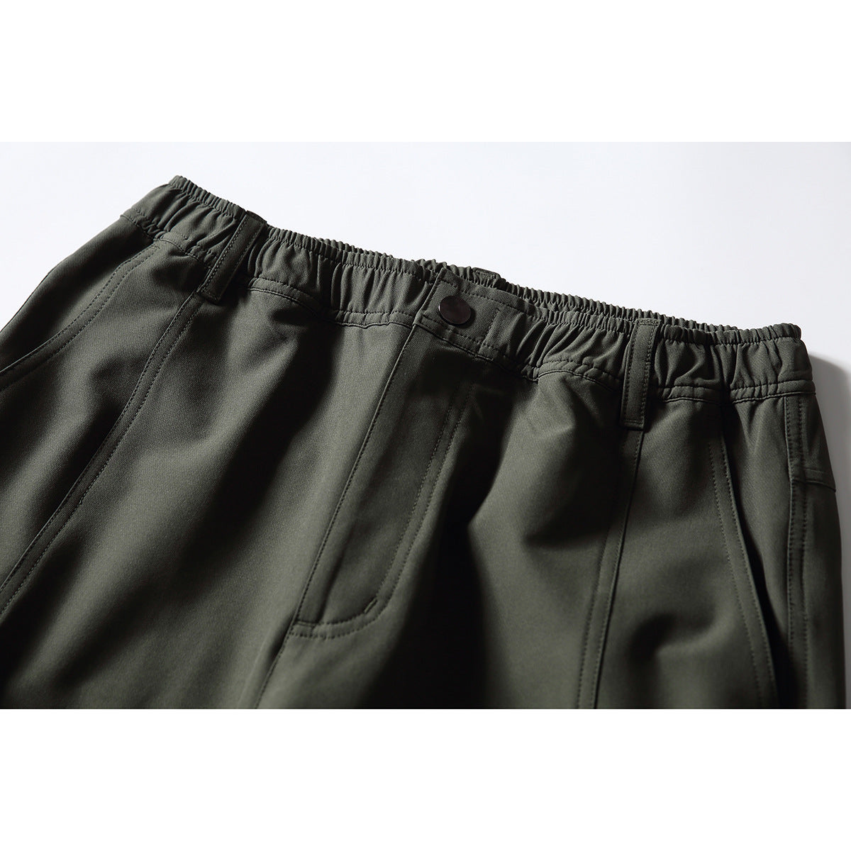 Close-up of dark olive pants showing the elastic waistband, button, belt loops, and front pocket.