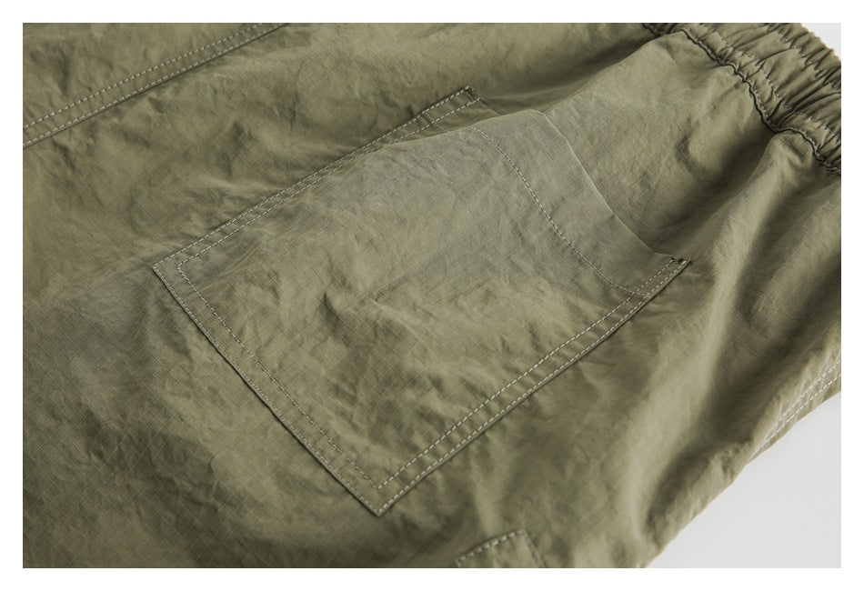 Close-up of a square patch pocket and double stitching on olive ripstop shorts.