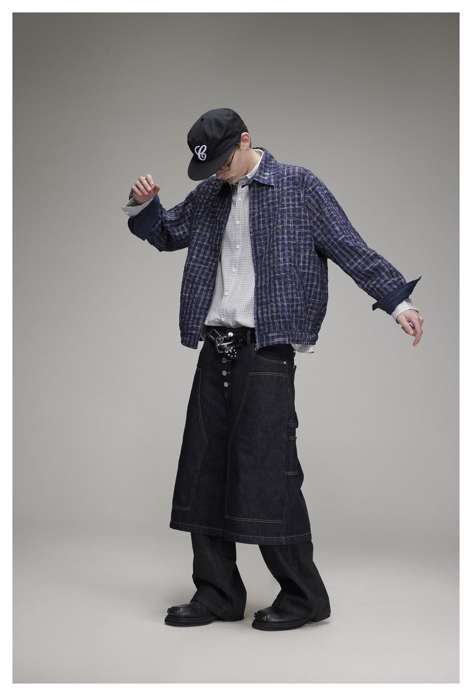 Model wearing a navy plaid jacket over a light checked shirt and dark wide-leg pants, shown at an angle.