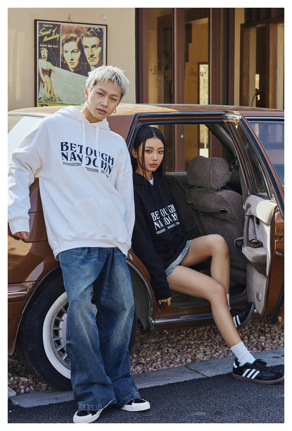 Two models wear oversized white and black graphic hoodies beside a vintage car; the white hoodie is shown full-length.