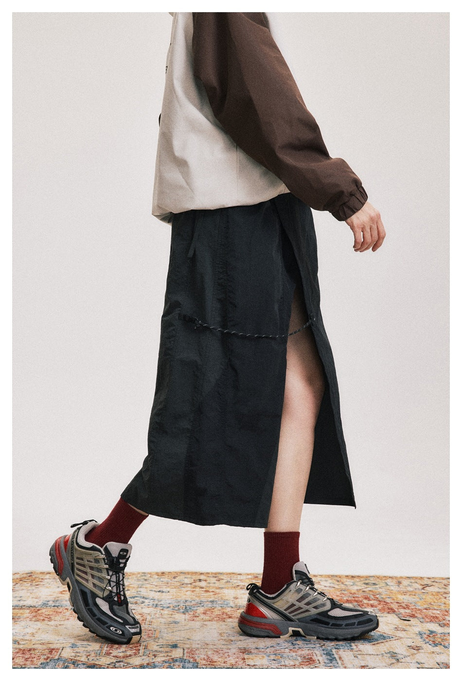 Side view of a model wearing a black mid-calf skirt with a high slit and cord detail.