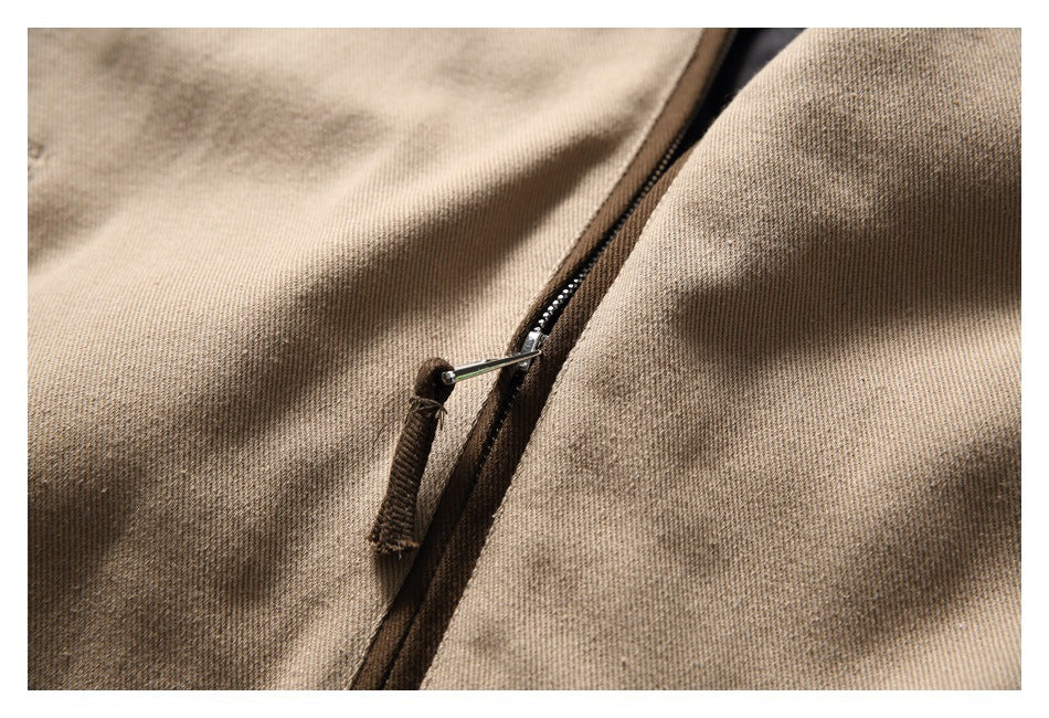 Close-up of a dark zipper and pull on tan textured garment fabric.