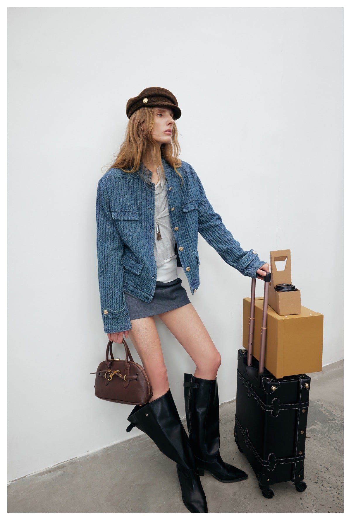 Model wearing a blue textured jacket with gold buttons and flap pockets, a gray skirt, and black boots.