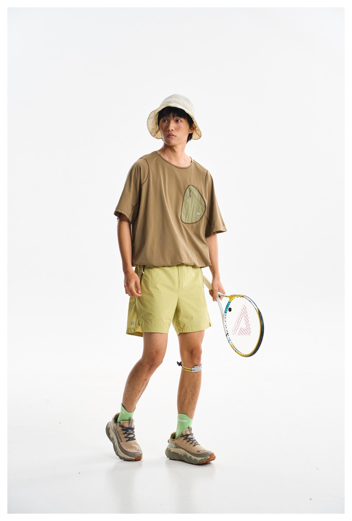 Model wearing a brown pocket T-shirt and light yellow-green shorts, shown from the front at an angle.