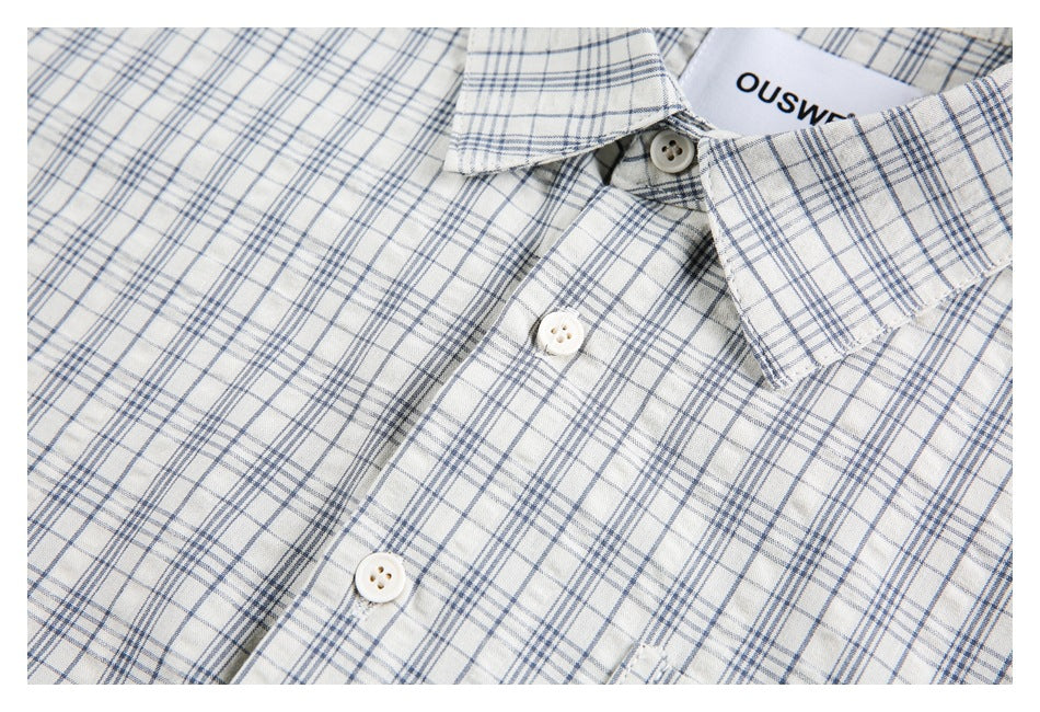 Close-up of the white and blue plaid shirt front, collar, buttons, and neckline label.