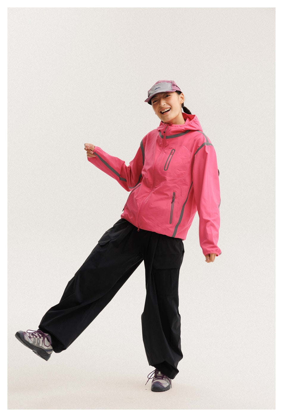 Model wearing a bright pink hooded jacket with gray trim and black cargo trousers, shown from the front at an angle.