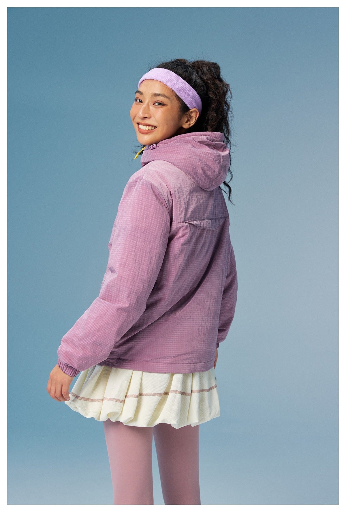 Rear view of a model wearing a lilac grid-pattern hooded pullover and white skirt.