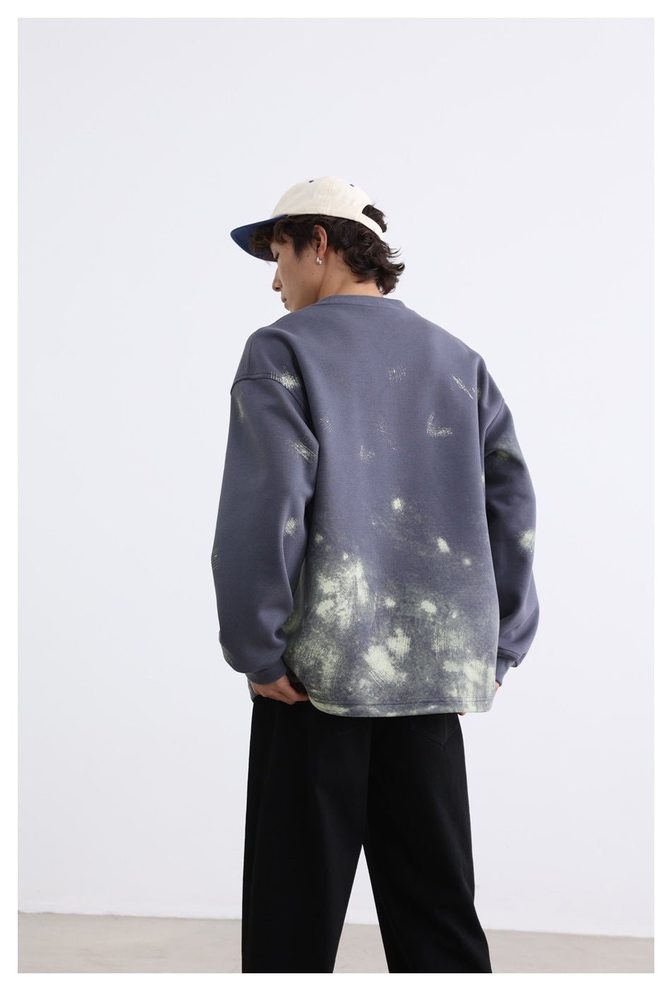 Model turned to show the back of a slate-blue oversized sweatshirt with pale distressed graphics.