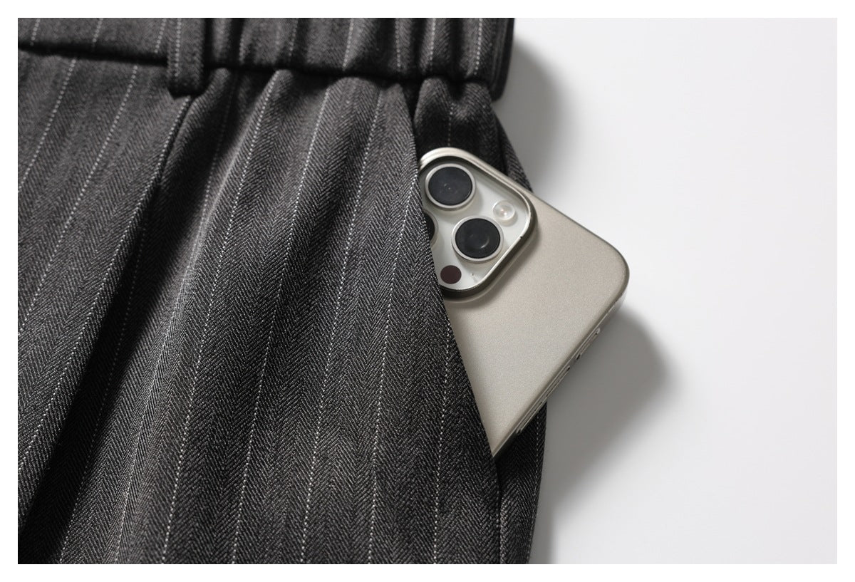 Close-up of a side pocket in charcoal pinstripe trousers with a smartphone tucked inside.