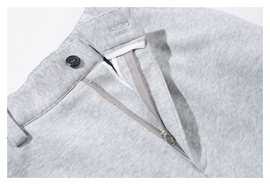 Close-up of light gray heathered pants showing the waistband button and partially open zip fly.