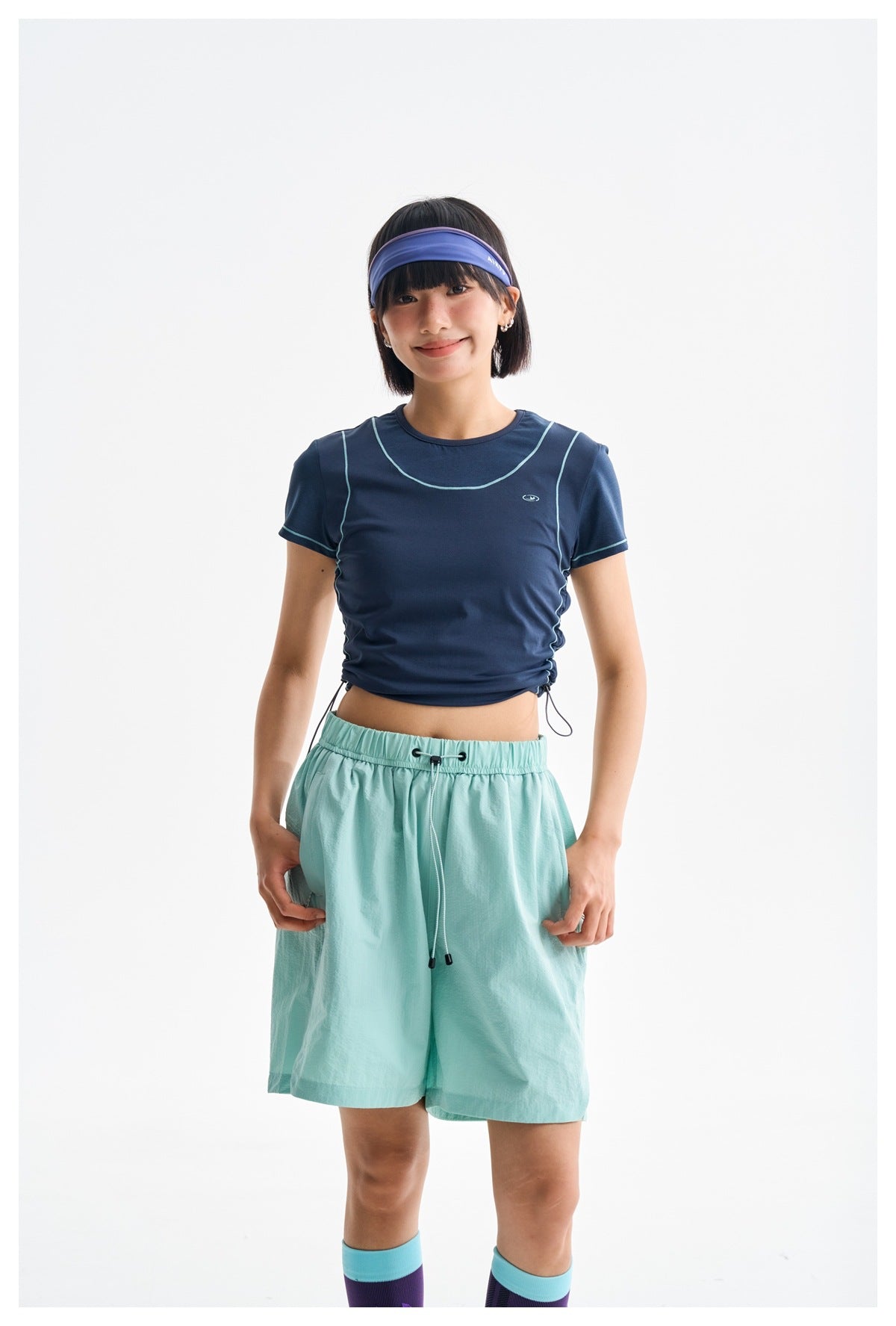 Front view of a model wearing a navy cropped T-shirt with pale piping and mint drawstring shorts.
