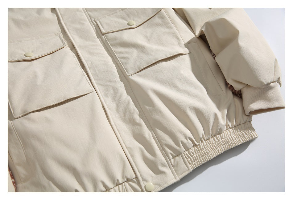 Close-up of the ivory jacket front, showing flap pockets, snap buttons, a gathered hem and a cuffed sleeve.