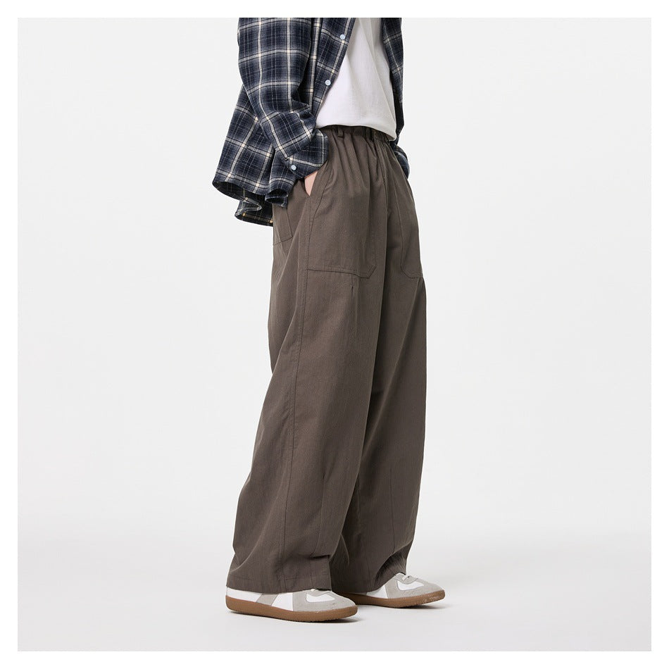 Side view of a model wearing dark taupe wide-leg trousers with an elastic waist and a navy plaid shirt.